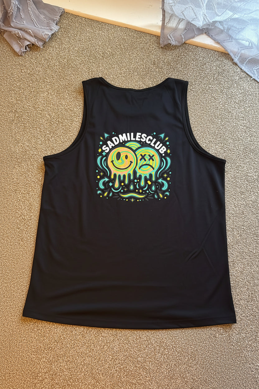 A black sleeveless tank top laid flat on a beige carpeted floor, featuring a colorful graphic on the back with two melting smiley faces and the text 'SADMILESCLUB'. A person's socked foot is visible at the bottom right of the frame.