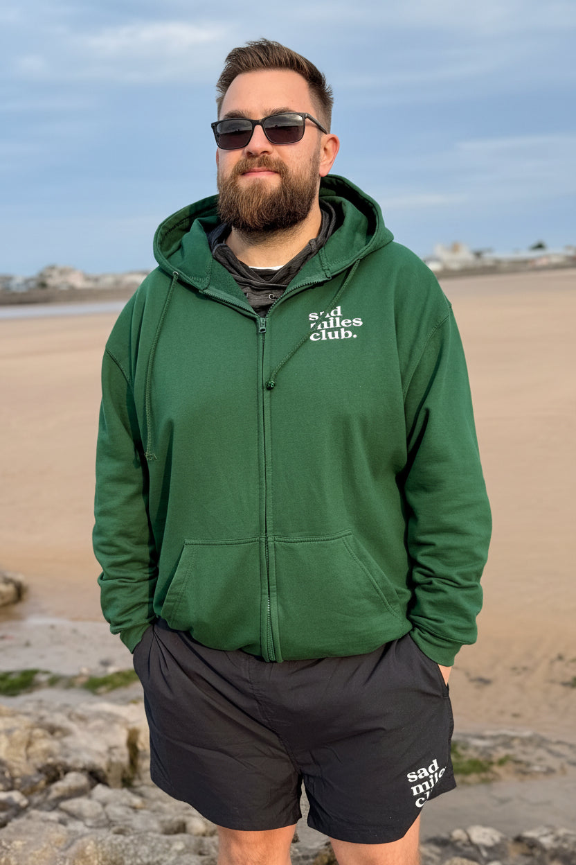 Man wearing a green hoodie with text on it, standing on a beach.