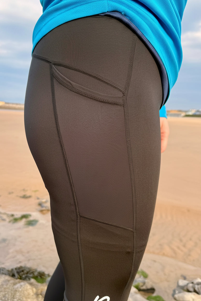 Black running leggings with a blue top worn by a person on a sandy landscape.