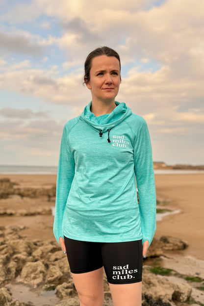 Person wearing a teal jacket and black shorts with text on a beach
