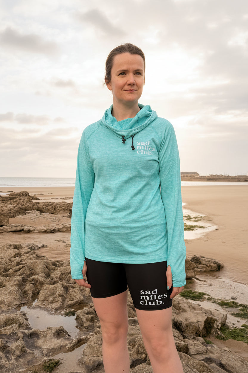 Person wearing a light blue jacket and black shorts with text on them, standing on a beach.