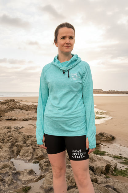 Person wearing a light blue jacket and black shorts with text on them, standing on a beach.