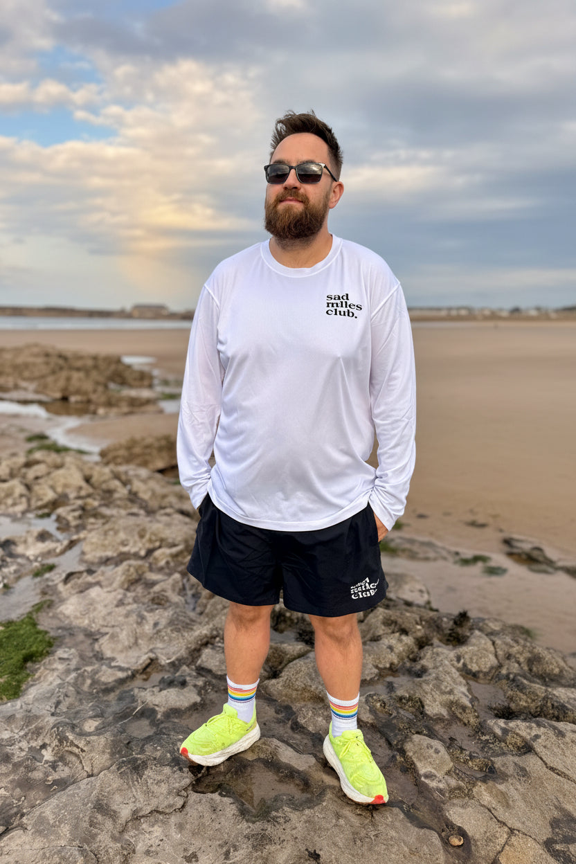 Man standing on a rocky beach wearing sunglasses and casual clothing.