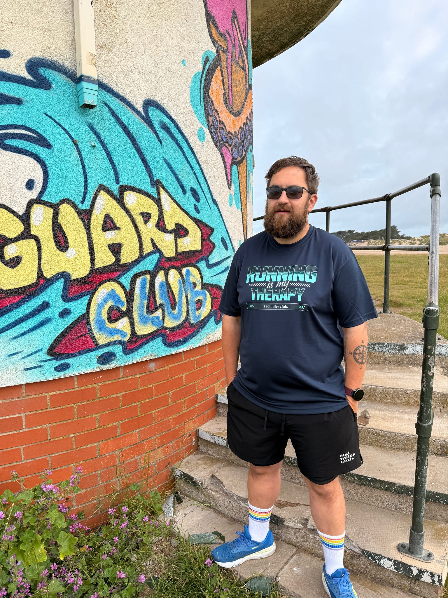 Man standing on steps in front of a colorful mural with 'Guards Club' text.
