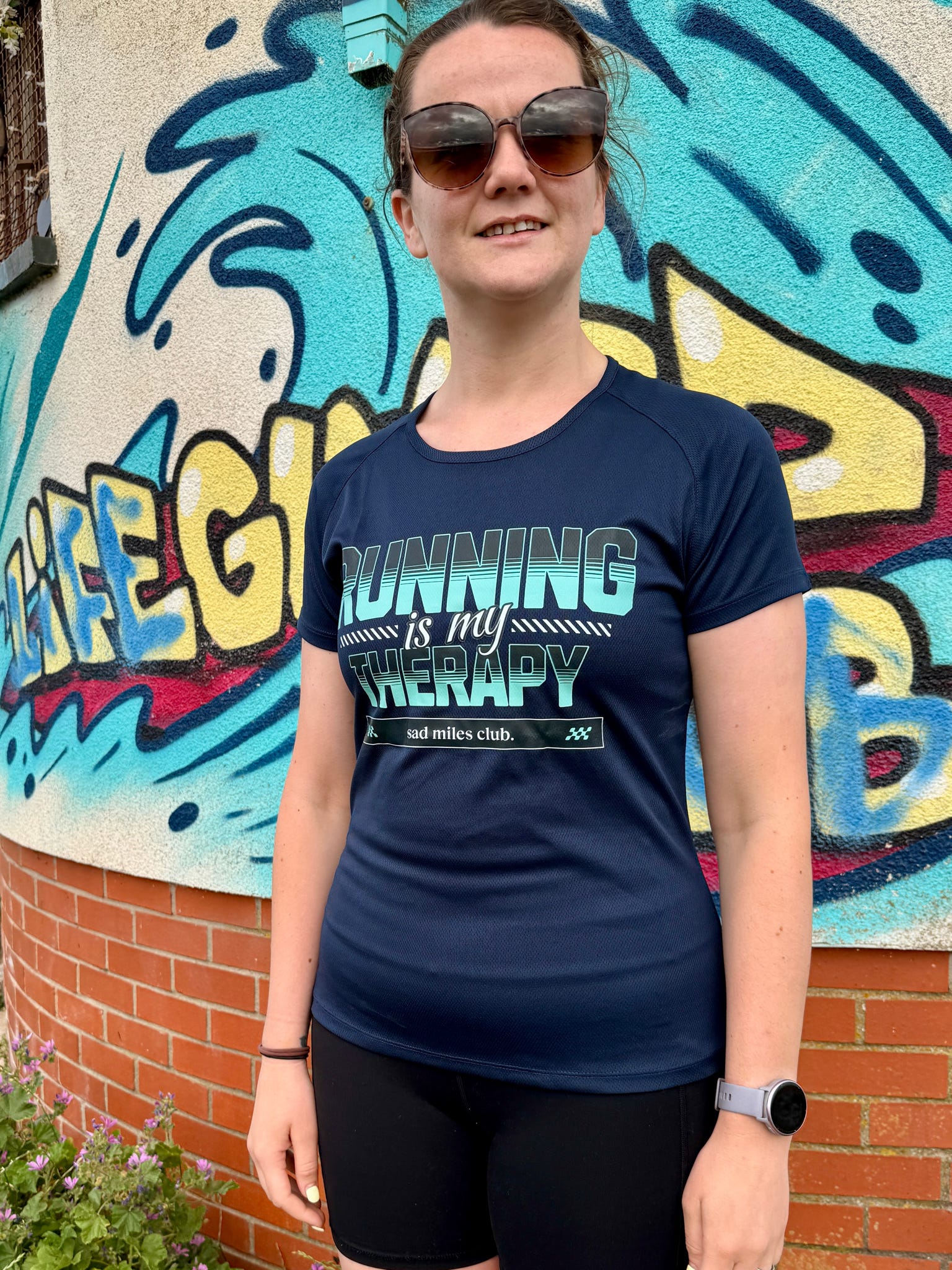 Person wearing a navy blue t-shirt with 'Running is my Therapy' text in front of a colorful mural.