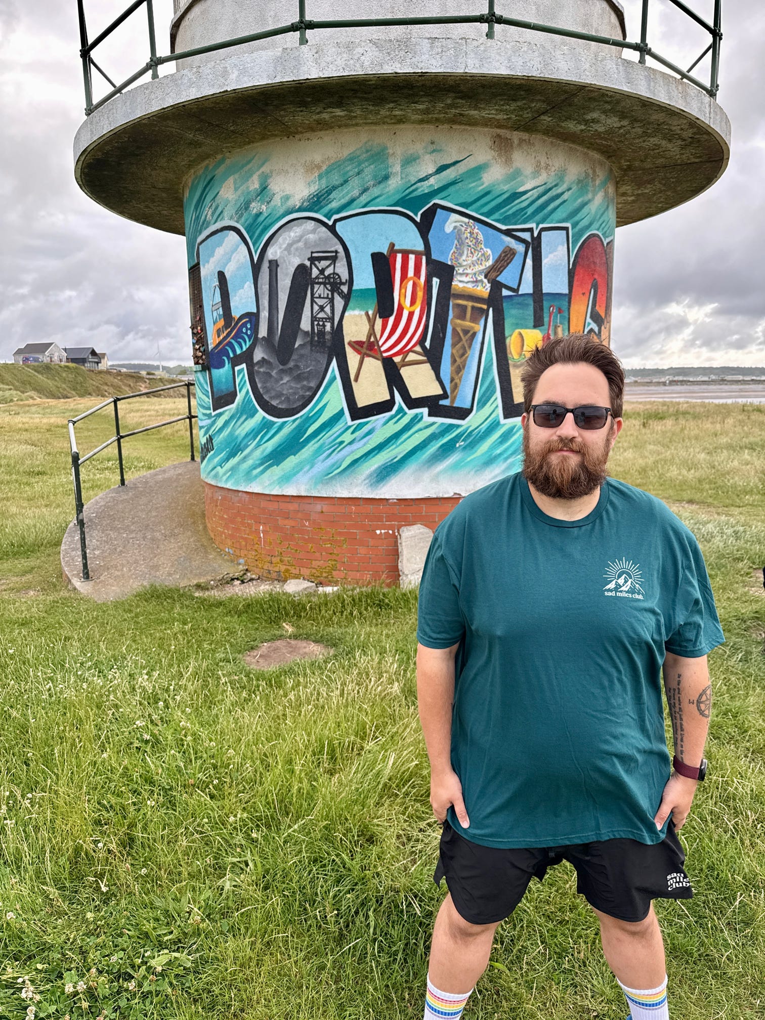 Man standing in front of a lighthouse with graffiti art on a cloudy day.