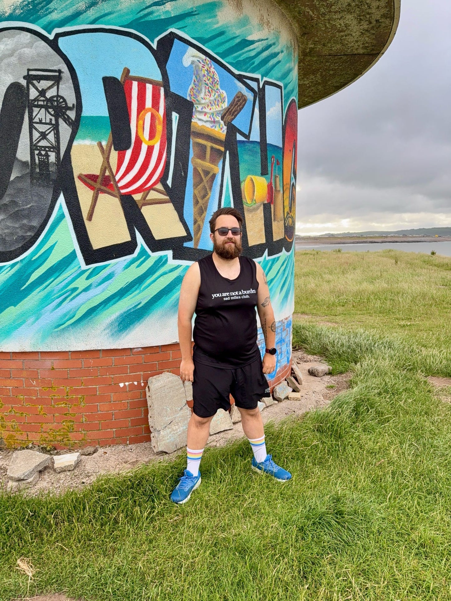 Man standing in front of a colorful mural with a scenic design on a brick wall.
